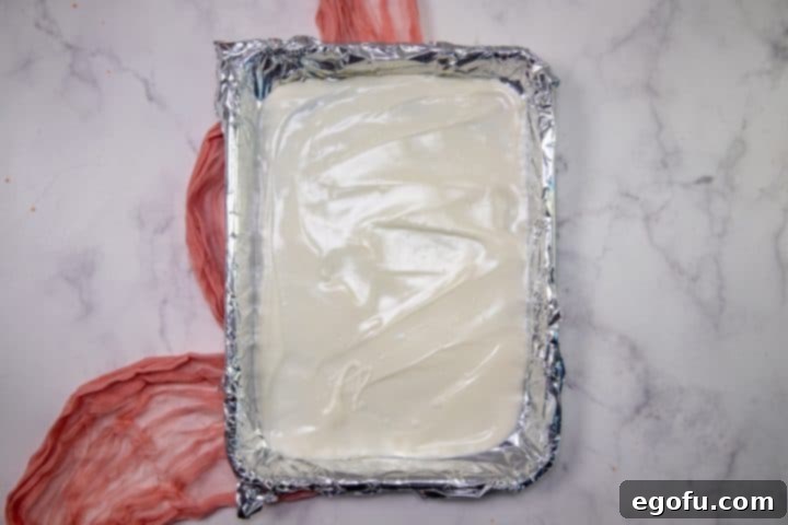 Cupids Oreo Bark 6 melted vanilla almond bark spread out on top of aluminum foil in a baking sheet.