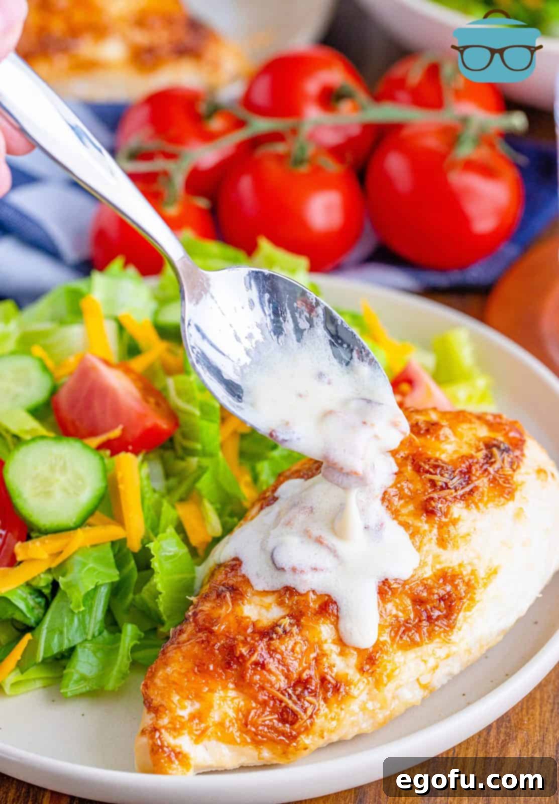 A spoon carefully drizzling the rich, creamy bacon sauce over a perfectly baked Parmesan chicken breast.