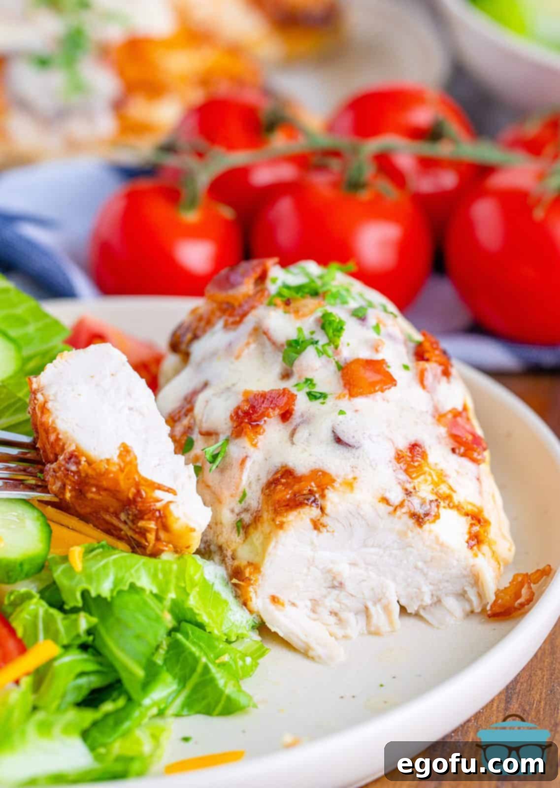 A cooked Parmesan chicken breast, cut open to reveal the moist, tender interior, topped with sauce and bacon crumbles.