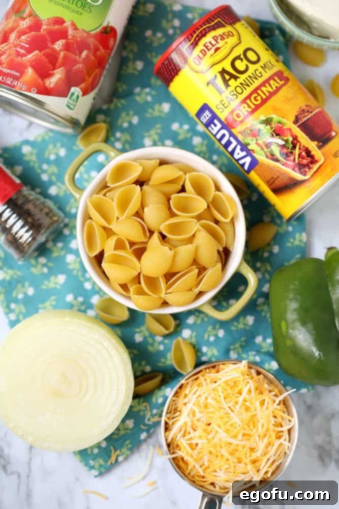 Assorted ingredients for Crock Pot Taco Pasta including pasta shells, taco seasoning, green peppers, diced tomatoes, shredded cheese, and diced onions.