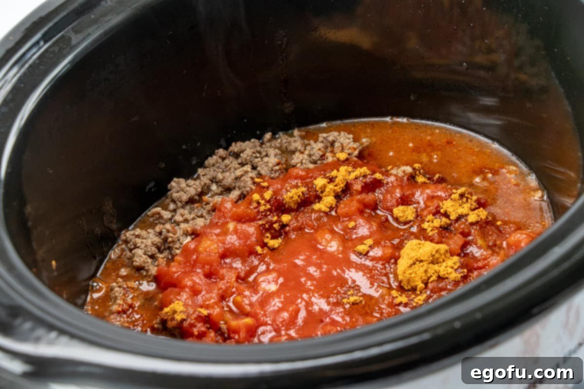 Cooked ground beef, diced tomatoes, water, and taco seasoning being combined in a slow cooker.
