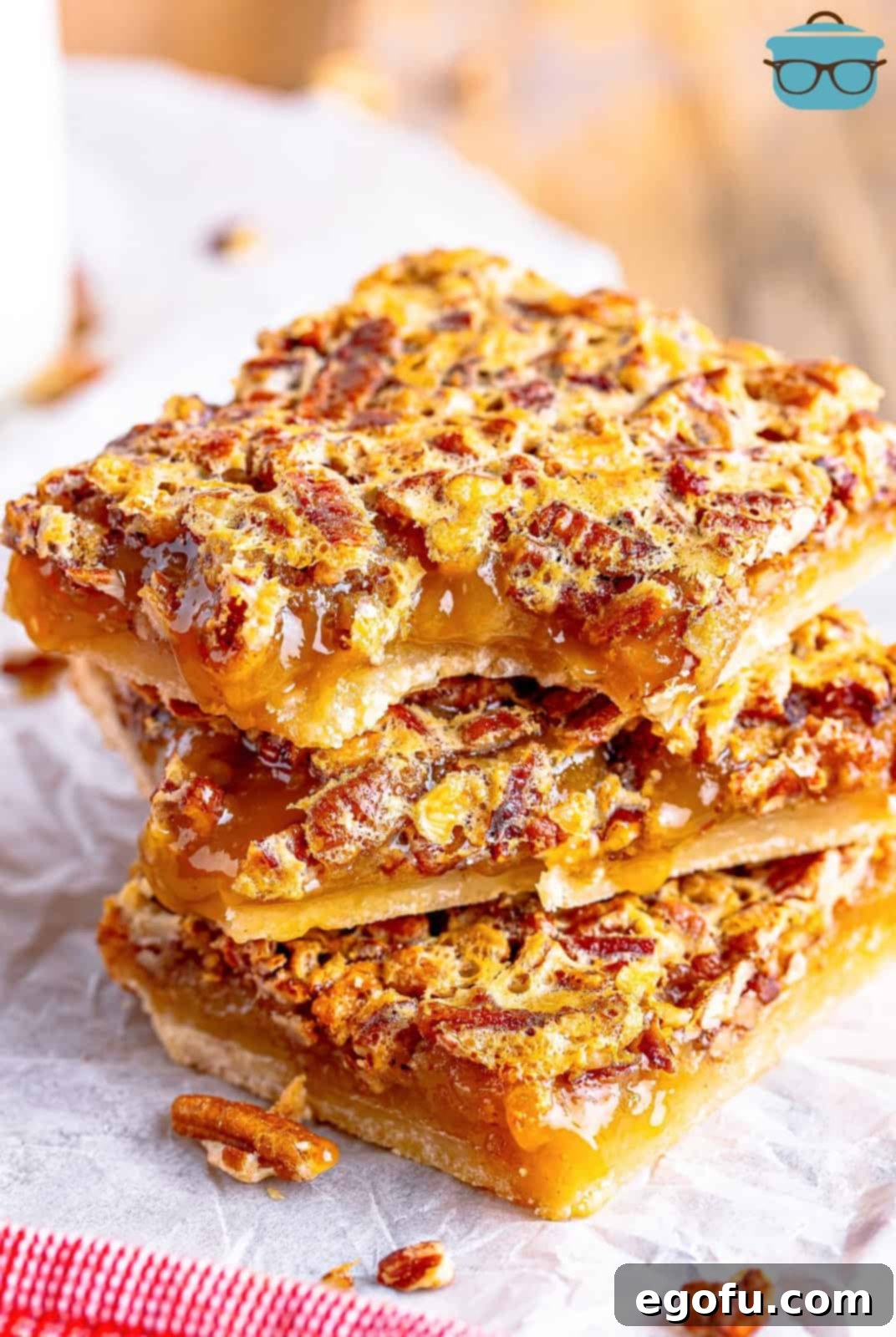 Three golden brown Southern Pecan Pie Bars stacked on parchment paper, with a bite taken out of the top bar, revealing the rich pecan filling and thick shortbread crust.