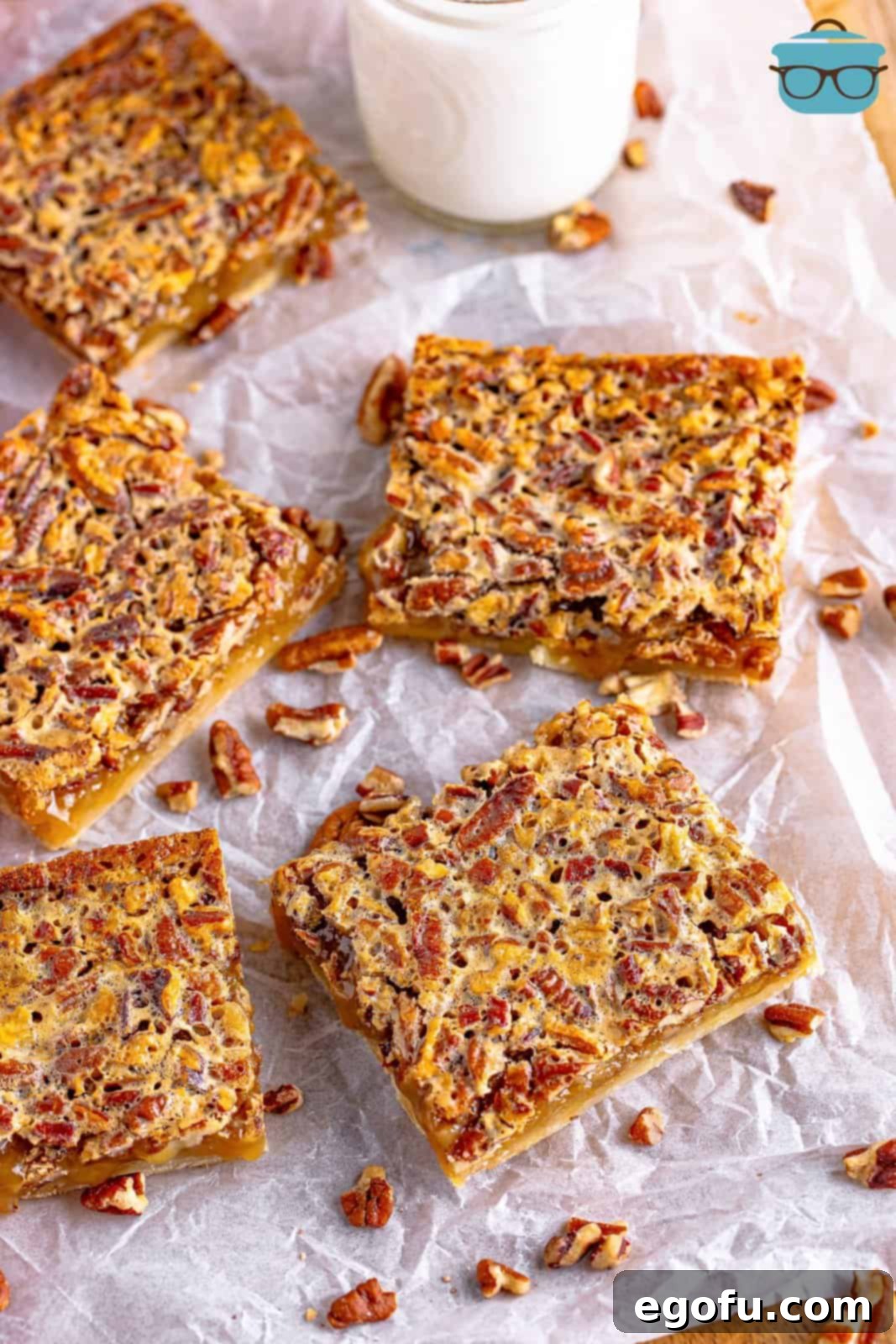 Five perfectly cut slices of Southern Pecan Pie Bars artfully arranged on white parchment paper, with a glass of milk blurred in the background, inviting a delicious tasting experience.