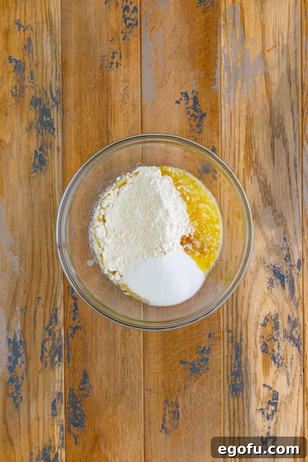 A large clear mixing bowl filled with the combined ingredients for the shortbread crust: butter, sugar, vanilla extract, and flour, mixed into a thick dough.