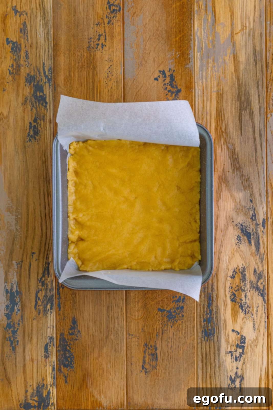 The buttery shortbread crust mixture evenly pressed into the bottom of a square metal baking pan, ready for its initial bake.