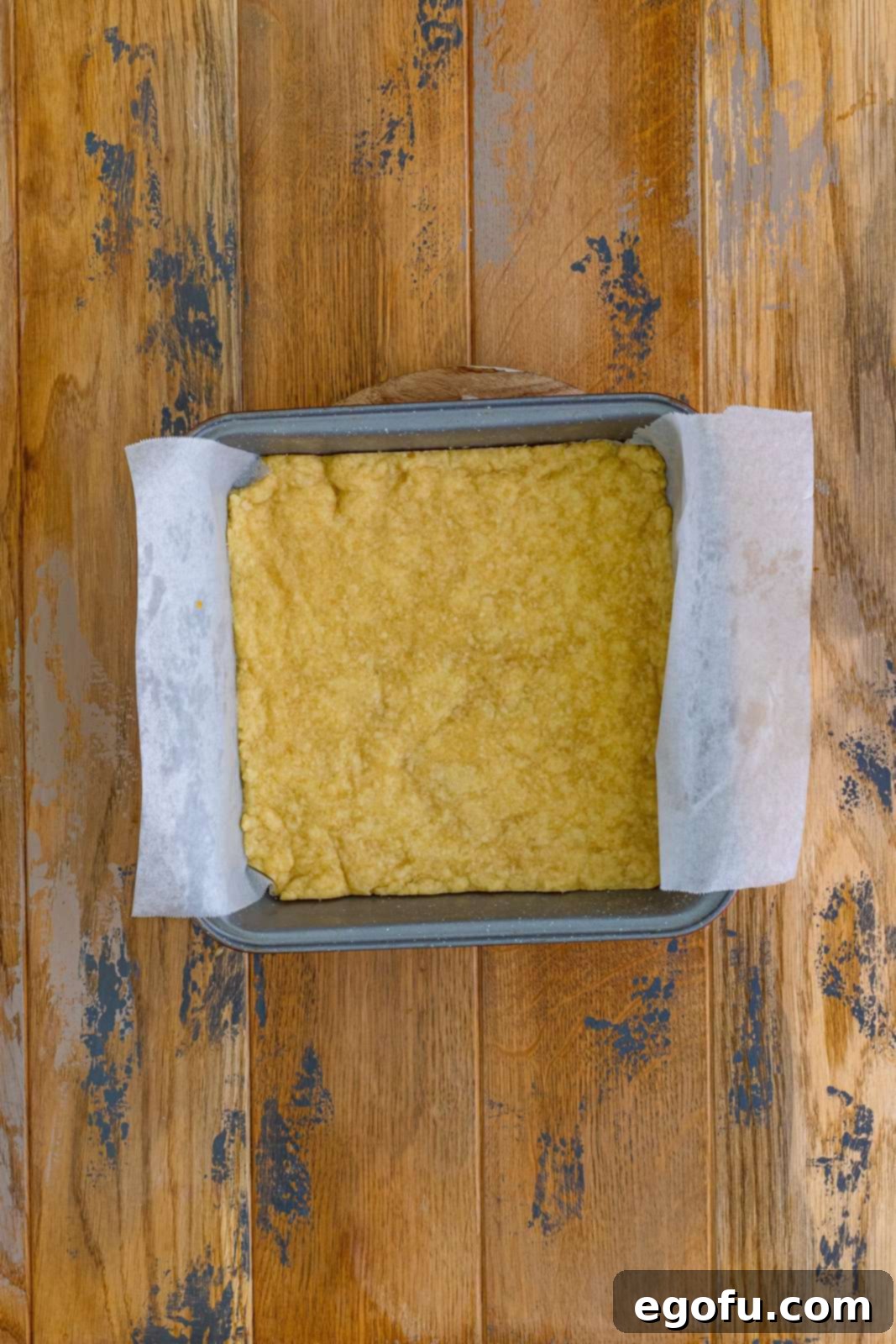 A partially baked golden shortbread pie crust sitting in the bottom of a metal square baking dish, showing its readiness for the pecan filling.
