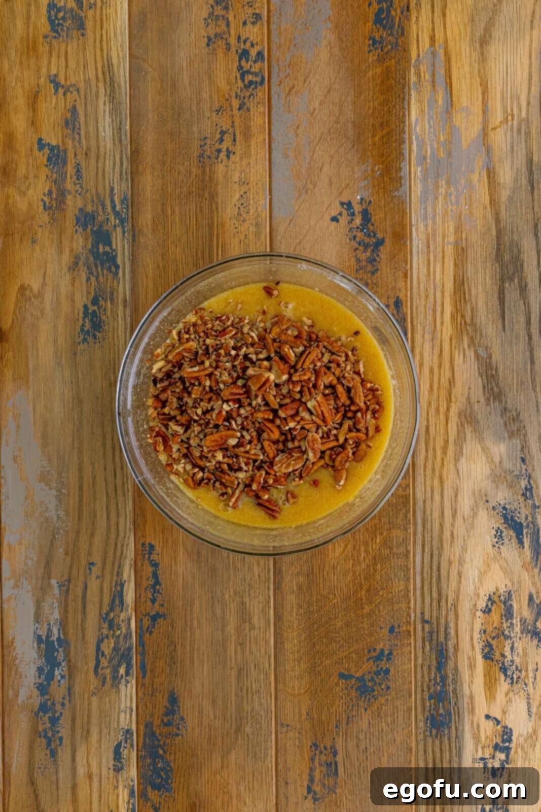 A clear mixing bowl holding the rich pecan pie filling mixture, featuring whole and chopped pecans, whisked eggs, brown sugar, and corn syrup, glistening and ready.