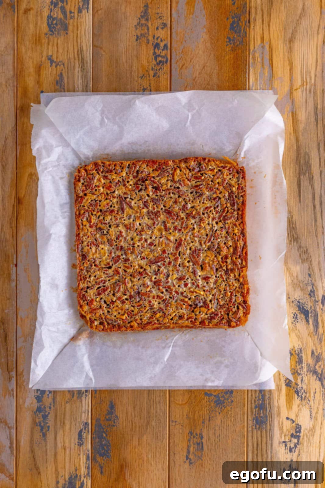 A batch of fully baked Southern Pecan Pie Bars, golden brown and perfectly set, resting on parchment paper after cooling.