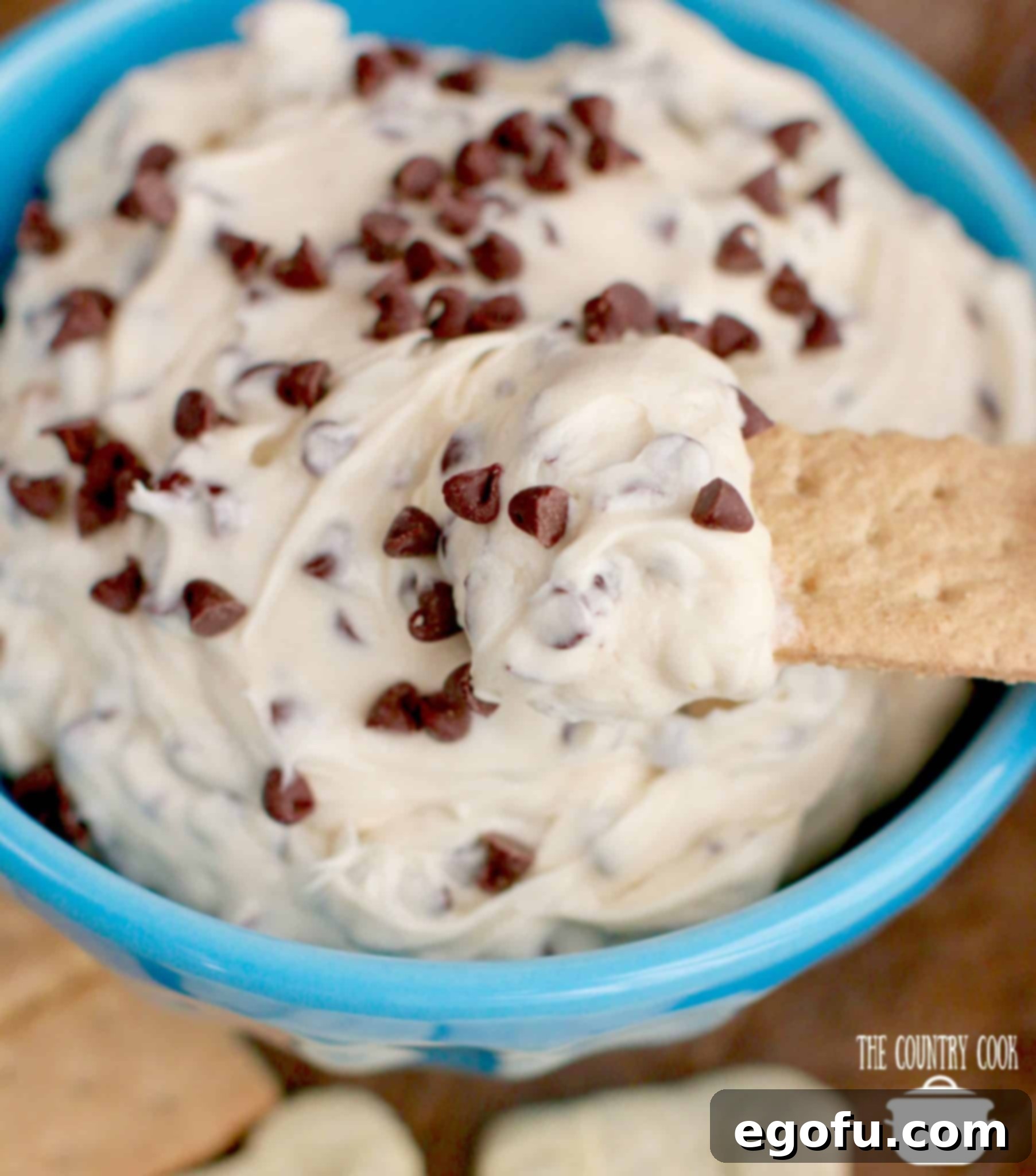 Decadent Chocolate Chip Dough Dip 4 A vibrant blue bowl filled with creamy Cookie Dough Dip, featuring a honey graham cracker ready for scooping.