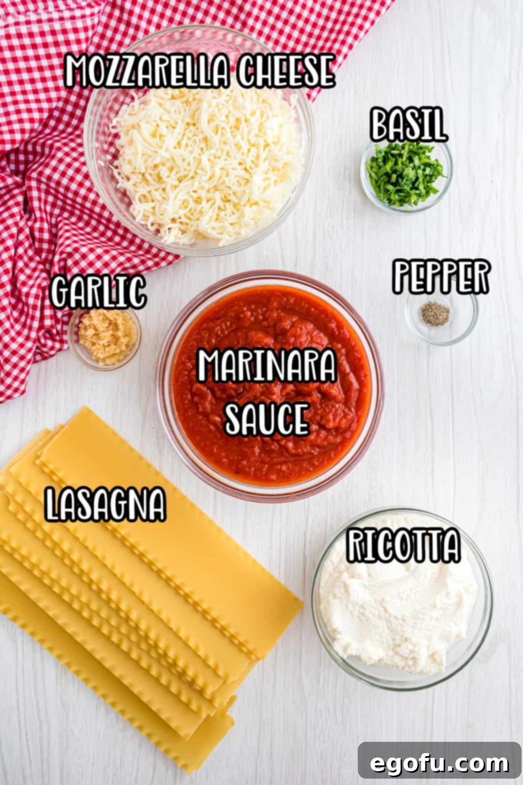 A vibrant flat lay of fresh ingredients including ricotta cheese, dried lasagna noodles, a jar of marinara sauce, fresh basil, minced garlic, and black pepper, ready for preparing lasagna roll ups.