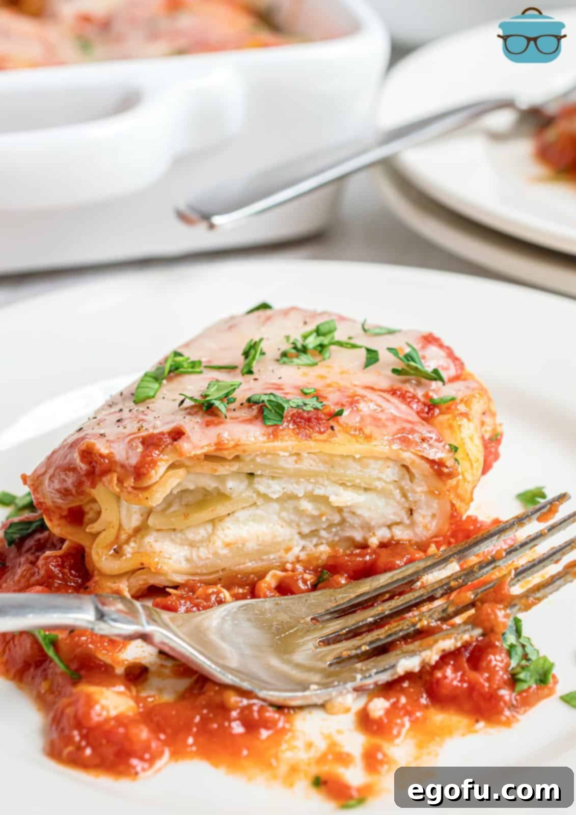 A single, perfectly baked lasagna roll up resting on a clean white plate, with a fork taking a bite, highlighting the layers of pasta, cheese, and sauce.