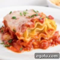 A closeup view of a lasagna rollup on a white plate, garnished with fresh basil.