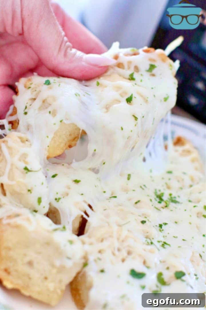 Hand pulling a piece of warm, cheesy garlic bread from a plate, highlighting its soft texture and melted cheese.