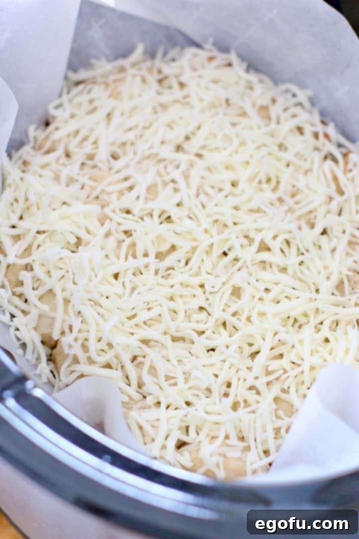 Shredded mozzarella cheese generously sprinkled over hot, cooked biscuits in the slow cooker, ready to melt.