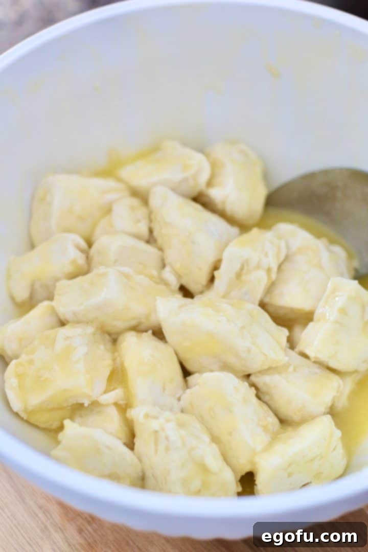 Biscuit pieces coated in melted margarine and minced garlic, tossed in a white bowl.