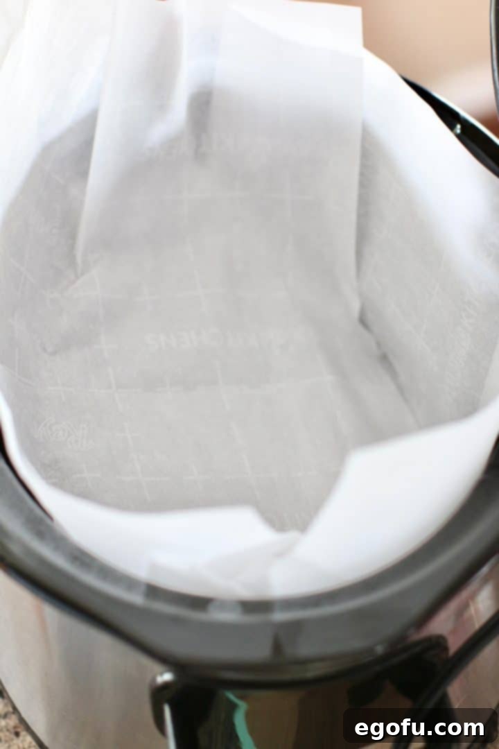 Parchment paper carefully lining the bottom of an oval slow cooker.