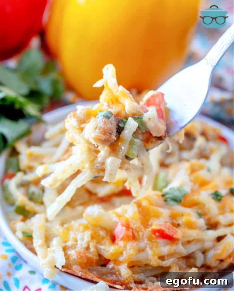 Lone Star Morning Spud Bake 2 A fork lifting a piece of golden-brown Texas Breakfast Hash Brown Casserole from a plate, showing the cheesy, peppery interior with hash browns and sausage.