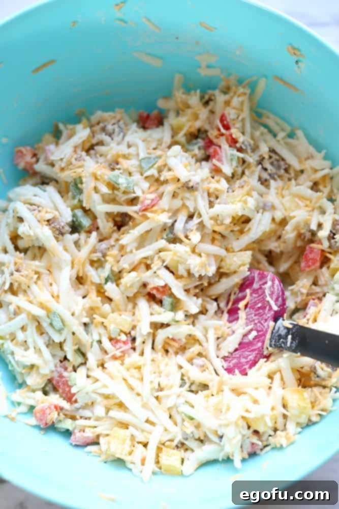 Lone Star Morning Spud Bake 5 A large mixing bowl filled with the combined core ingredients for Texas Breakfast Hash Brown Casserole: hash browns, diced green, red, and yellow bell peppers, crumbled cooked sausage, heavy cream, cumin, salt, and pepper, ready to be mixed thoroughly.