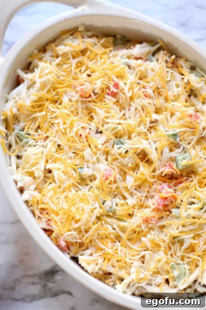 Lone Star Morning Spud Bake 6 Unbaked Texas Hash Brown Casserole in a baking dish, with the hash brown mixture spread evenly and topped with a generous layer of shredded Mexican cheese, ready for the oven.