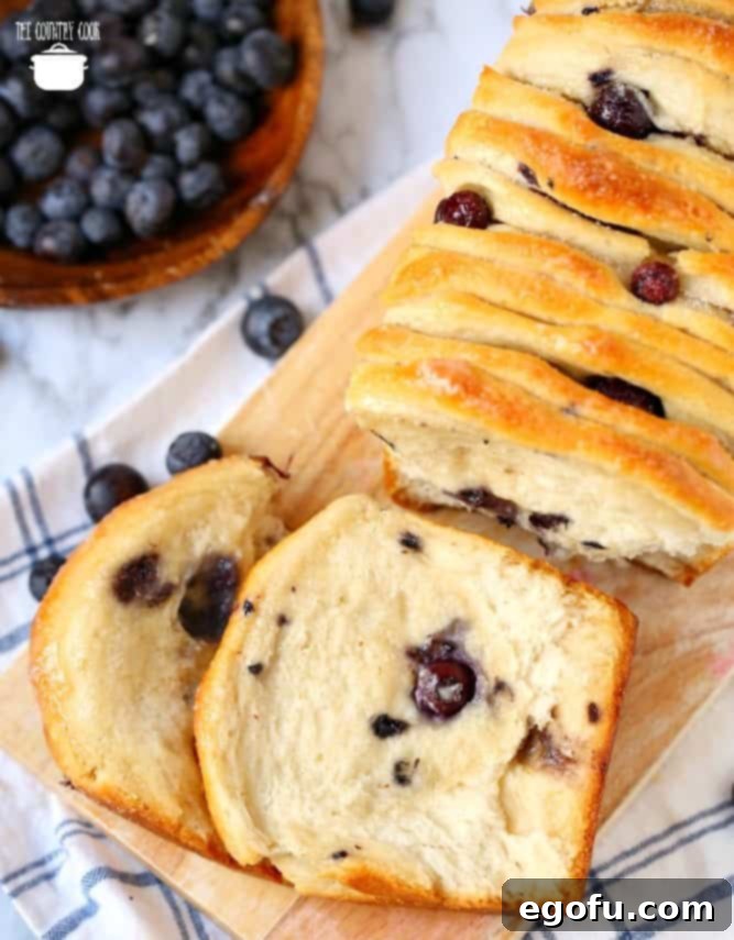 Heavenly Blueberry Tear & Share 2 Blueberry Pull Apart Bread, with fresh blueberries, slices on a light wooden cutting board.