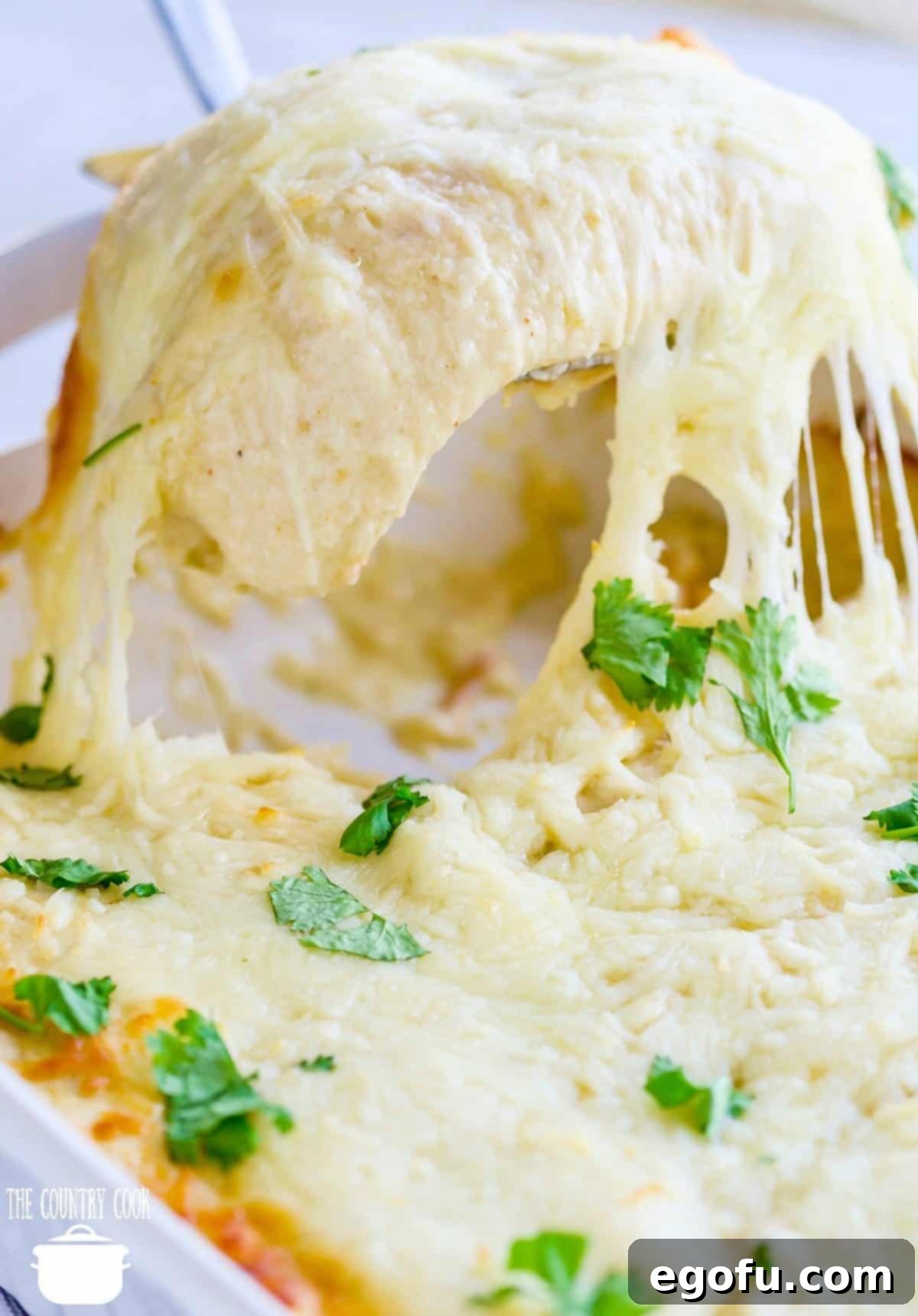 a spatula scooping out to enchiladas from a white baking dish.