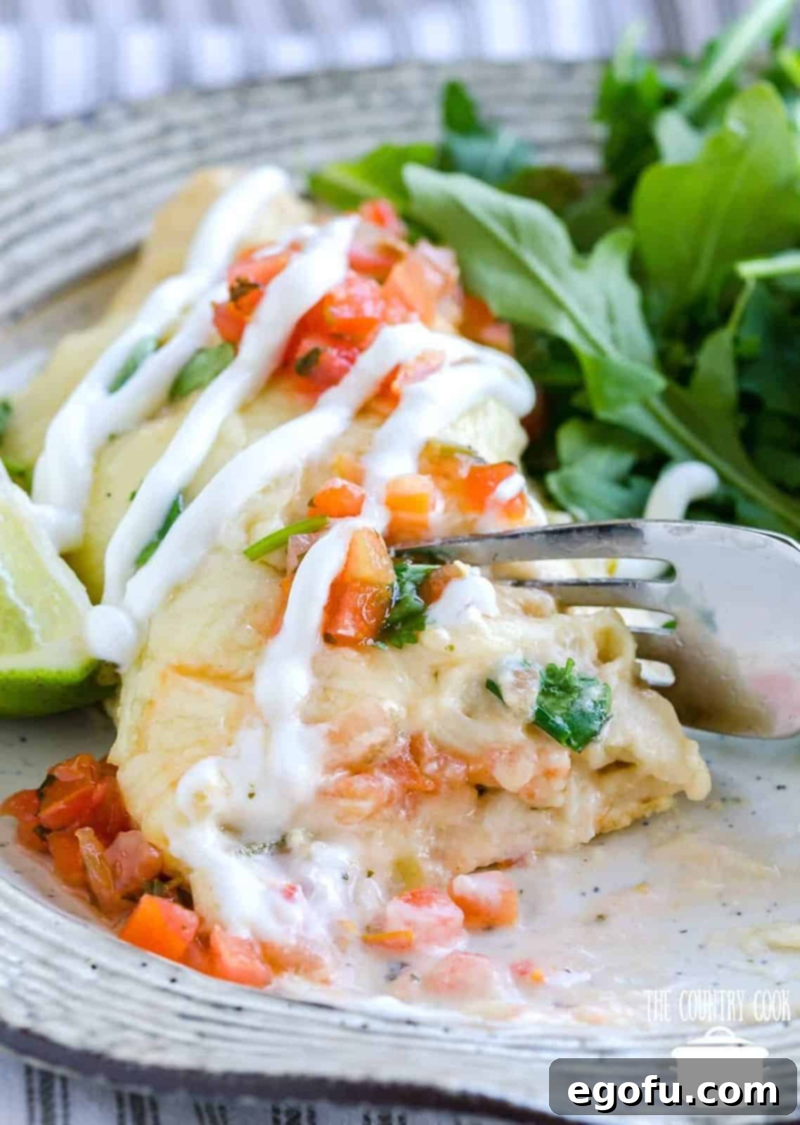 a fork slicing into a shrimp enchilada on a plate.
