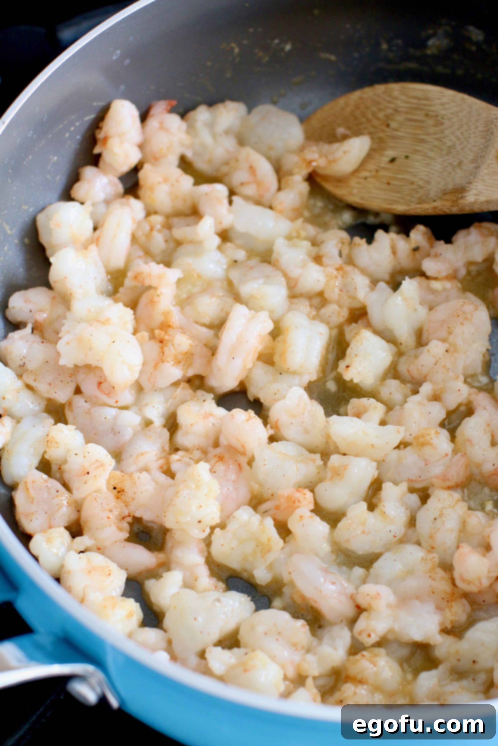 cooking shrimp in a skillet with a wooden spoon.