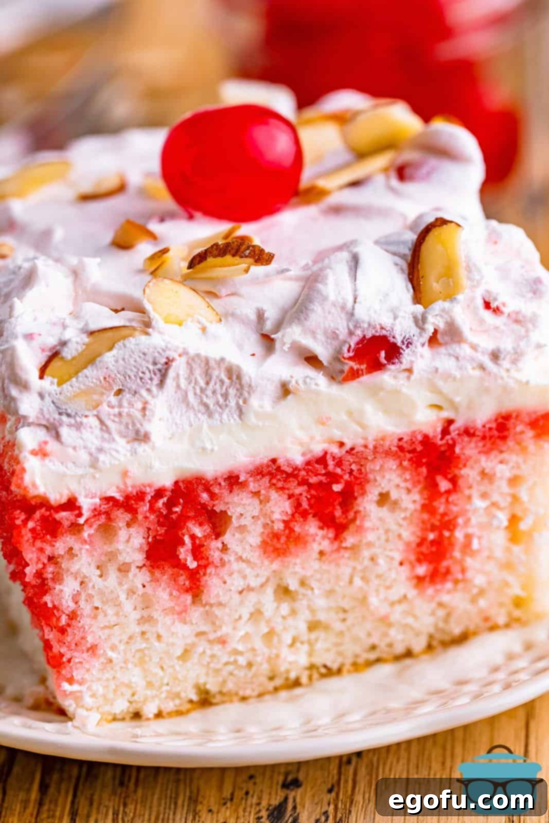 close up side photo of cherry almond poke cake on a small round white plate.