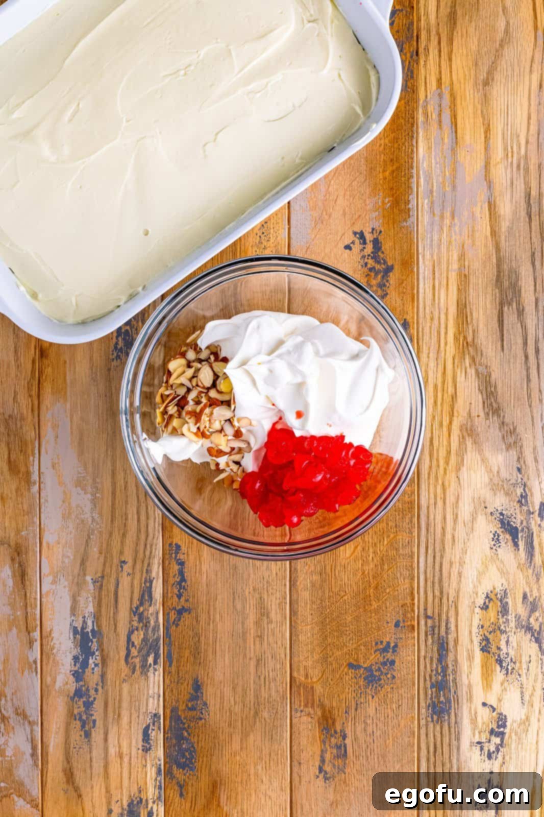 whipped topping, maraschino cherries and slivered almonds in a bowl.