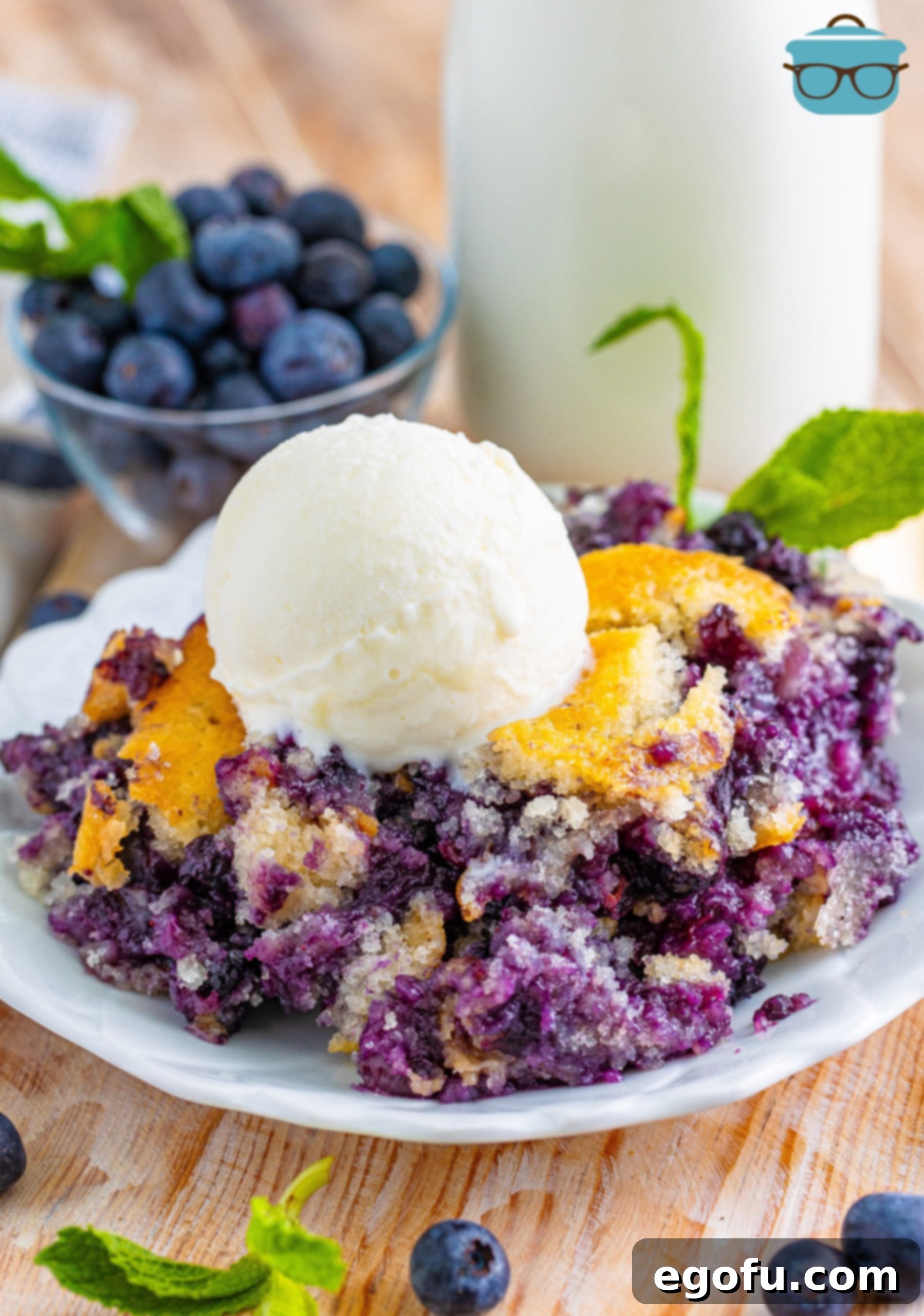 serving of blueberry cobbler in a white plate with a scoop of vanilla ice cream on top.