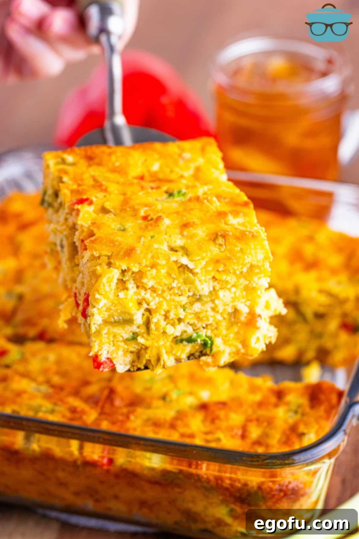A serving utensil holding a large slice of Mexican Cornbread above the rest of the baking dish.