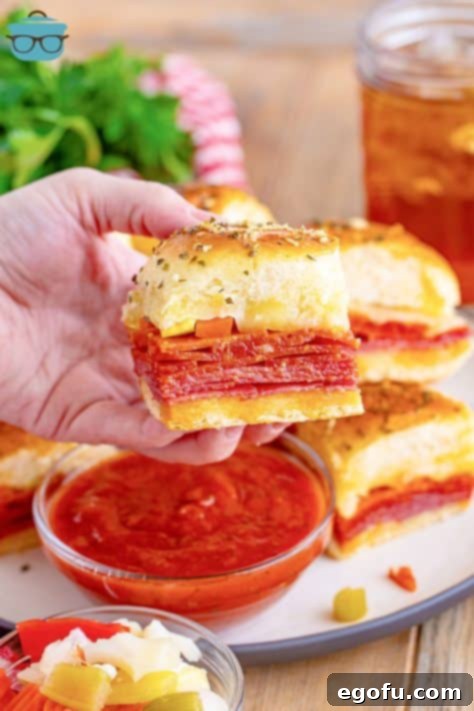 A hand holding an Italian Slider above some sauce and more sliders.