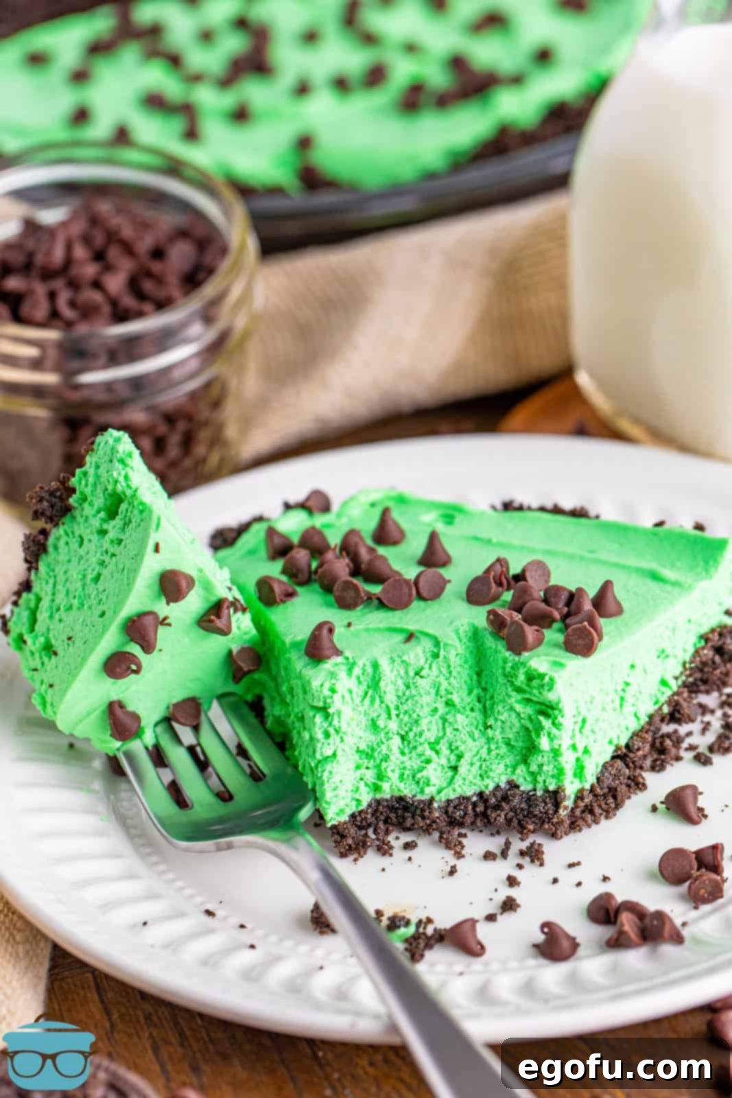A perfectly sliced piece of green grasshopper pie on a white plate with a bite removed, revealing the creamy texture.