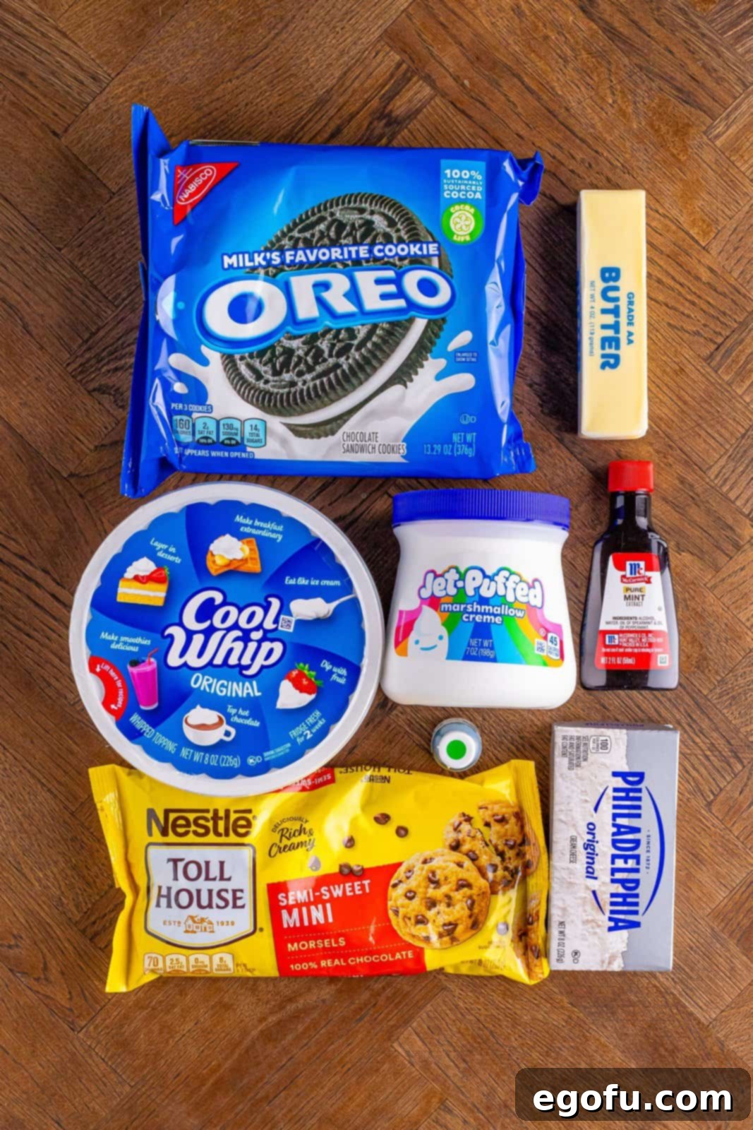A flat lay photograph showcasing all the ingredients for Grasshopper Pie: Oreo cookies, whipped topping, mint extract, green food coloring, marshmallow fluff, butter, and mini chocolate chips.