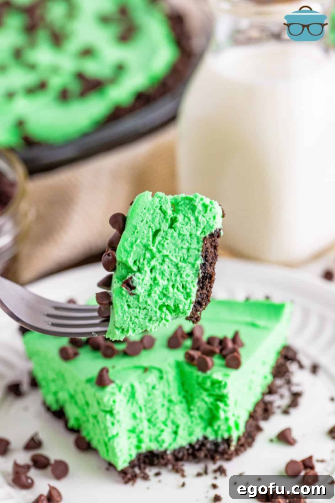 A fork holding up a perfect piece of Grasshopper Pie, with a glass bottle of milk subtly blurred in the background, hinting at a delightful pairing.