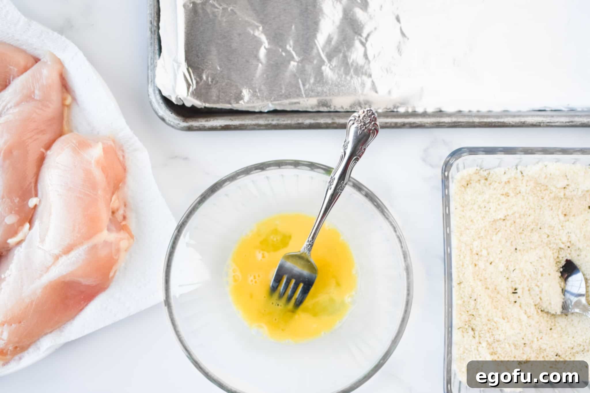 chicken breasts, sheet pan, egg yolk and panko bread crumbs in a dish.