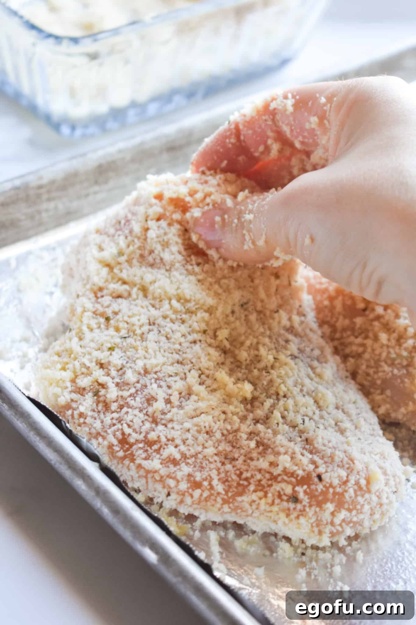 coated chicken breast being places on baking sheet.