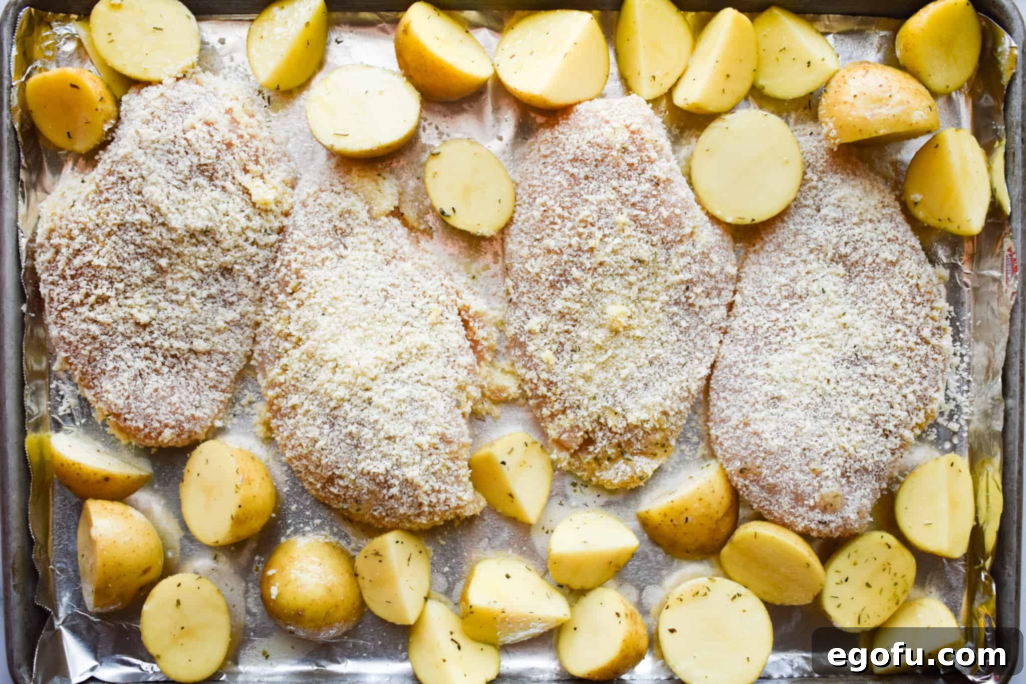 coasted chicken breasts and seasoned sliced potatoes on a large baking sheet.