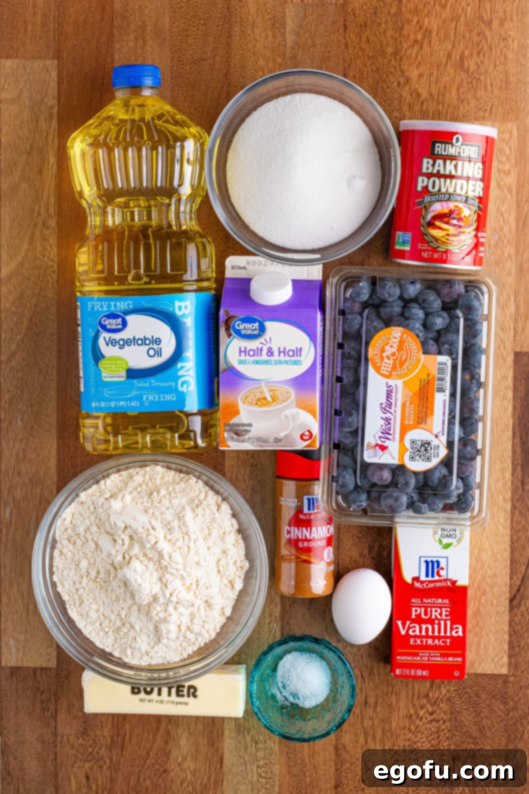 Sweet Blueberry Streusel Cake 4 An array of fresh blueberries, half and half, all-purpose flour, granulated sugar, baking powder, an egg, vanilla extract, and cinnamon are neatly arranged on a surface, highlighting the core ingredients for the buckle.