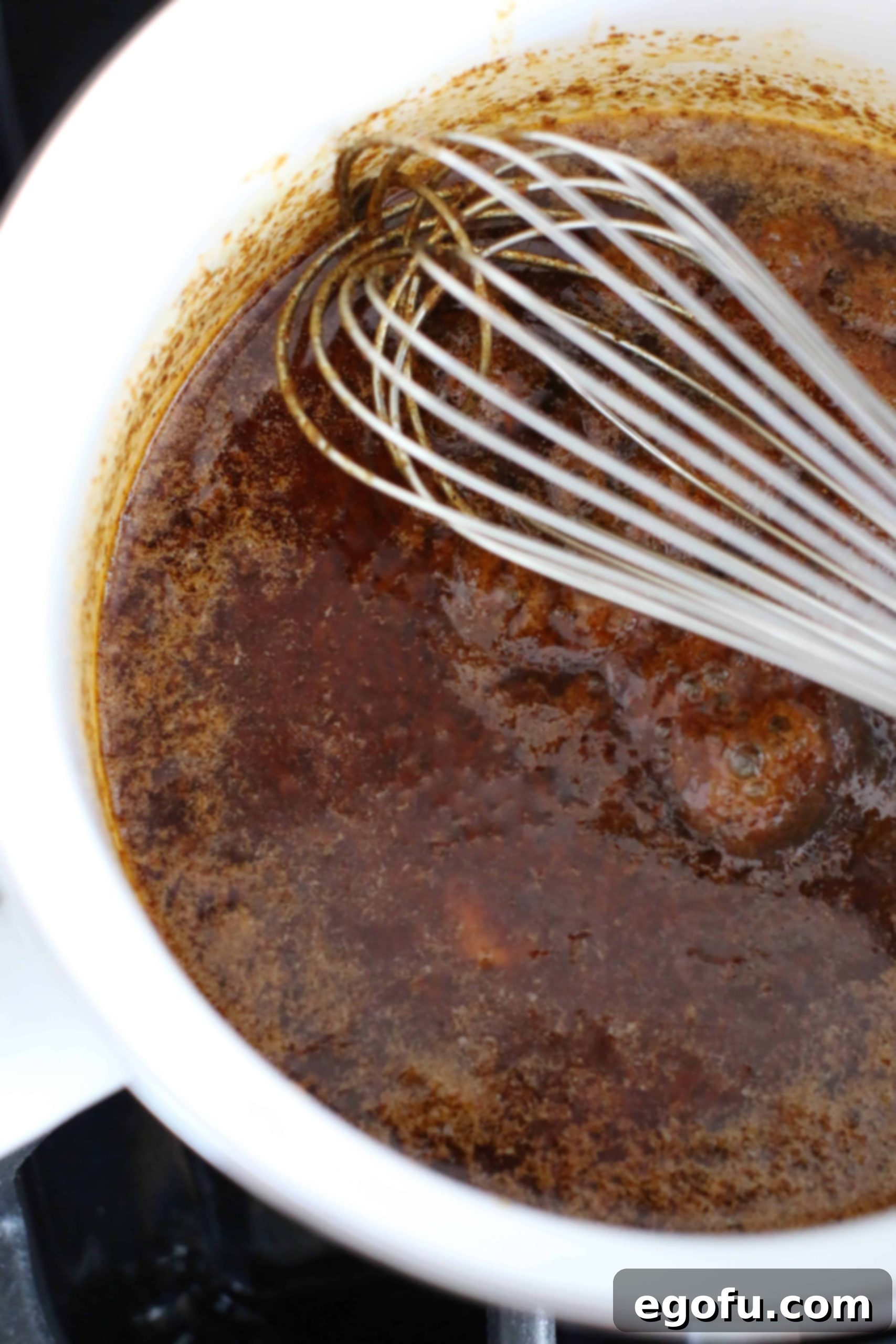 Nashville hot chicken sauce being whisked in a white pot, showing the vibrant spice blend with oil.