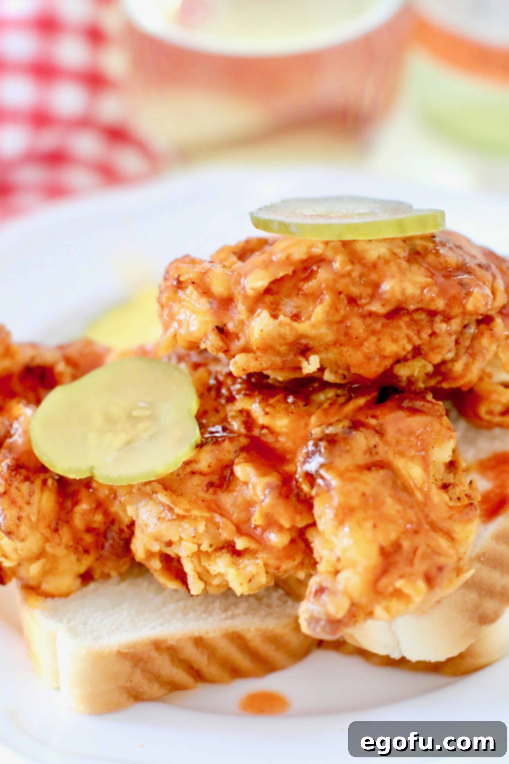 Nashville Fried Hot Chicken pieces on slices of white bread with sliced pickles on top, beautifully presented.