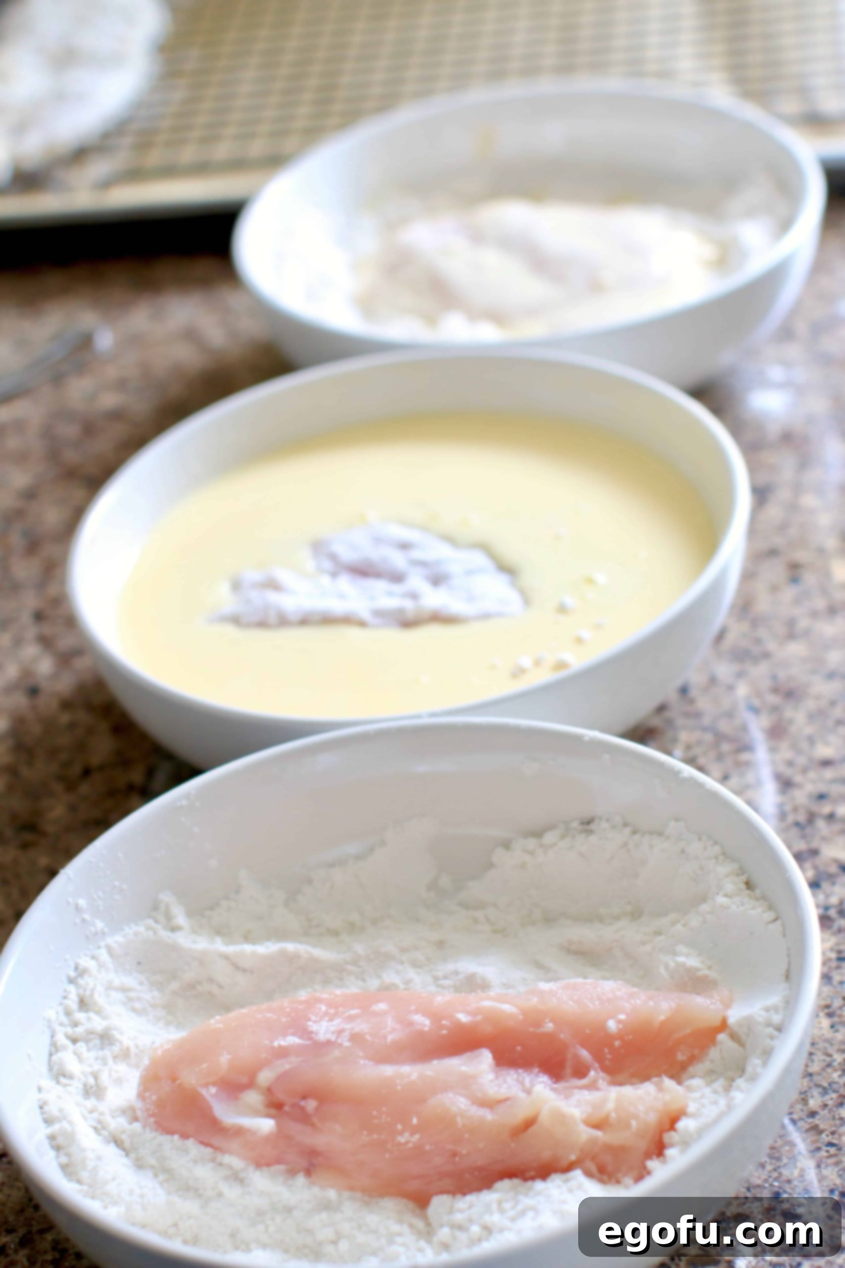 Coating chicken breasts in three bowls, showing the dredging process.