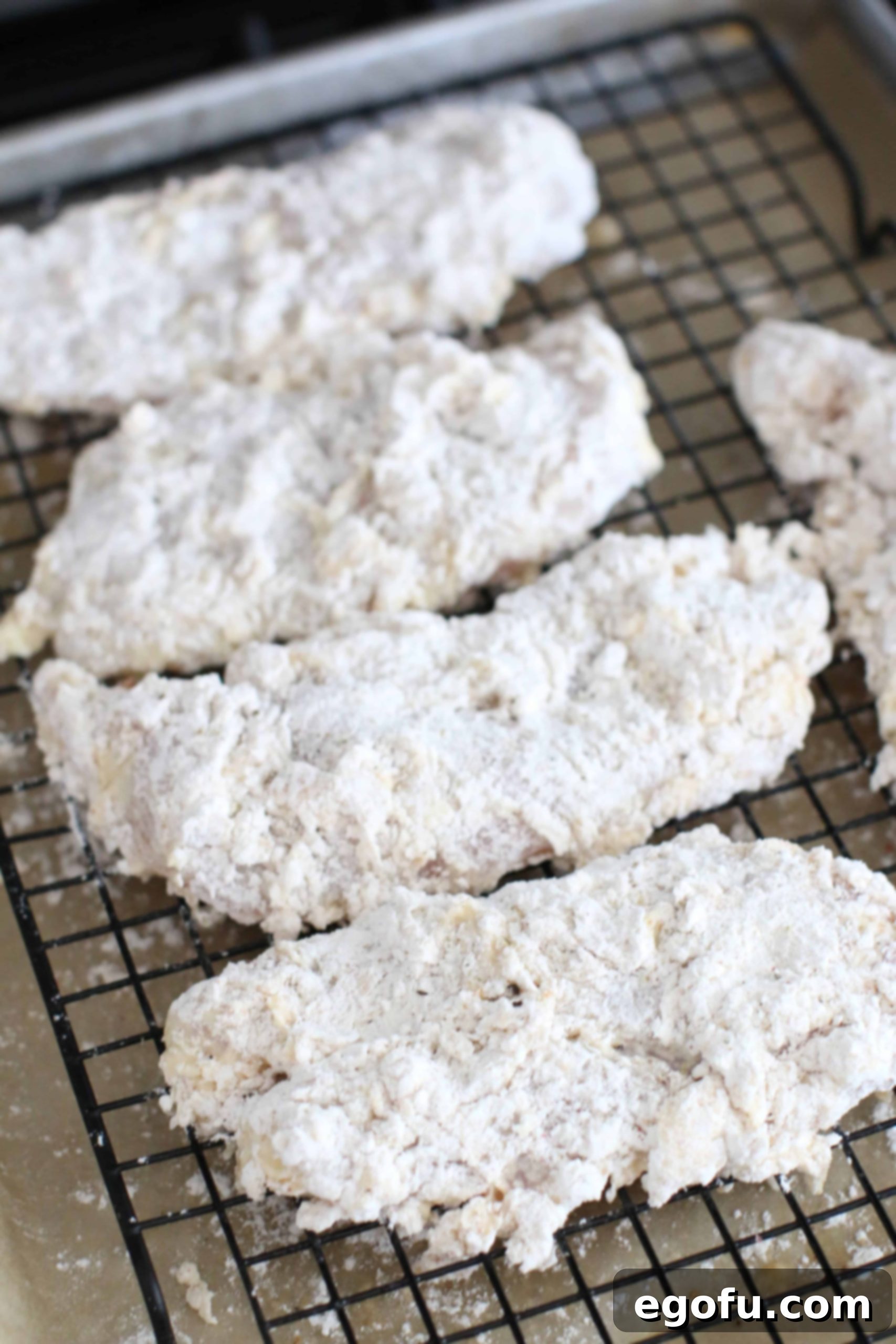 Prepared chicken breasts on a baking sheet, coated and ready for frying.