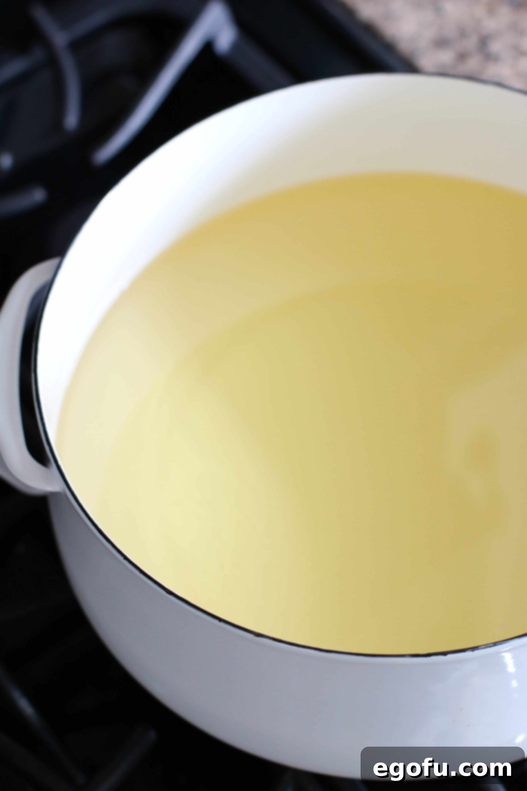 Peanut oil heating in a white Dutch oven pot on a gas stove, preparing for frying.