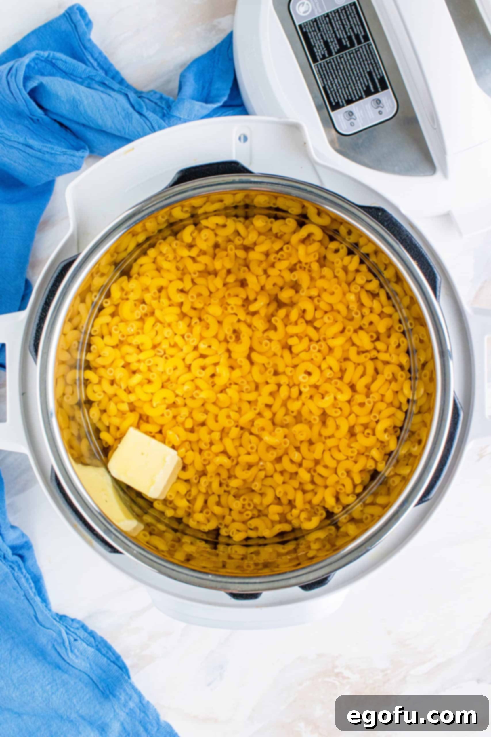 Uncooked macaroni noodles, butter, and water in the bottom of an Instant Pot electric pressure cooker, ready for cooking.