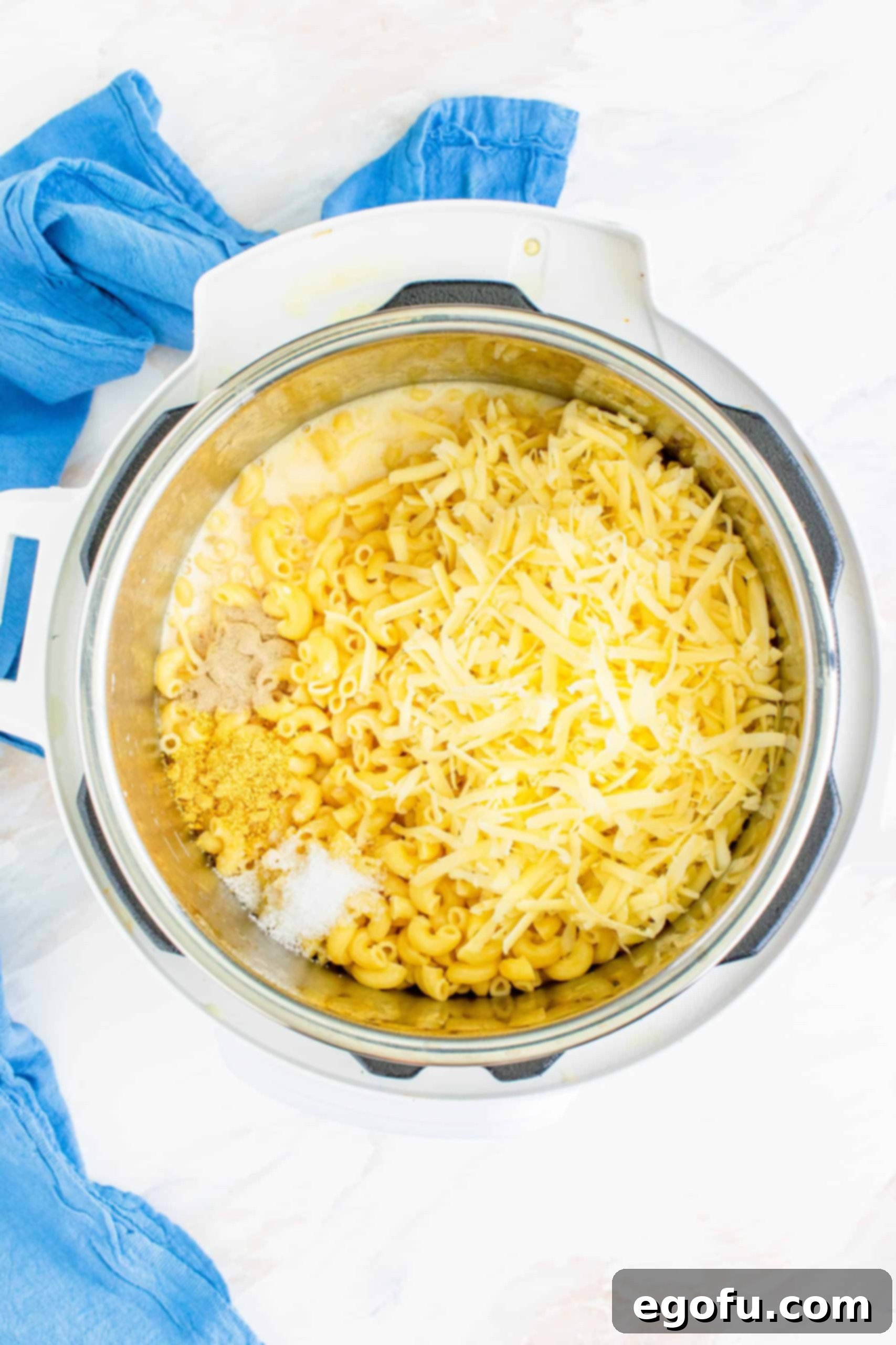 Evaporated milk, salt, pepper, and shredded cheese added on top of cooked elbow macaroni noodles in the Instant Pot.