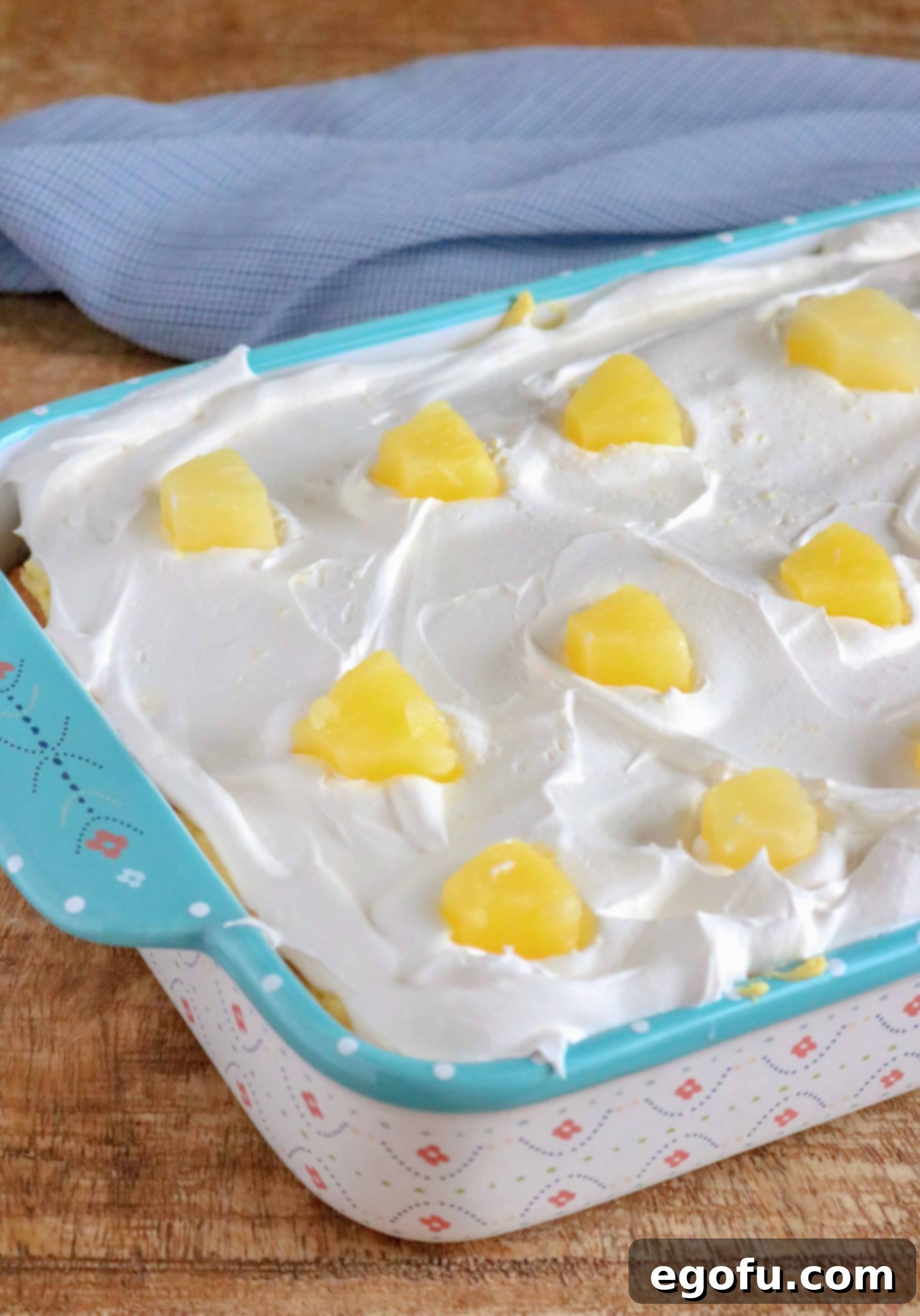 A close-up of the finished Pineapple Pudding Poke Cake, generously topped with fluffy Cool Whip and bright pineapple chunks, ready for chilling.
