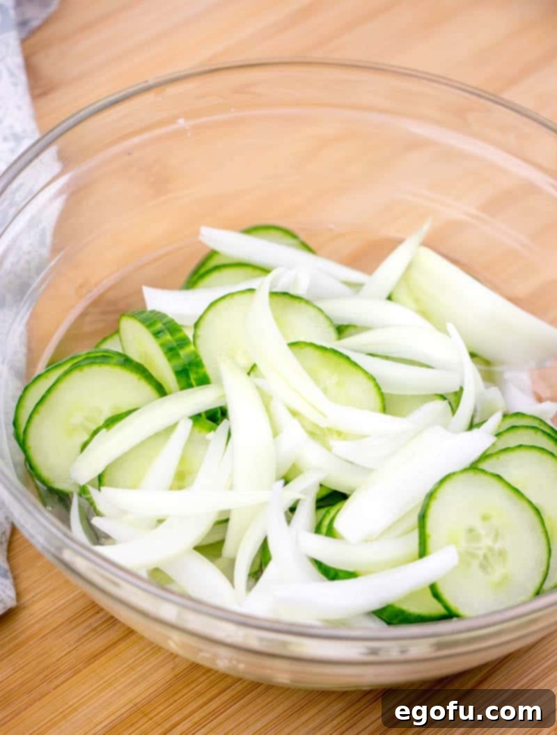 Sliced cucumber and onion in a bowl, seasoned with salt and ready for vinegar.