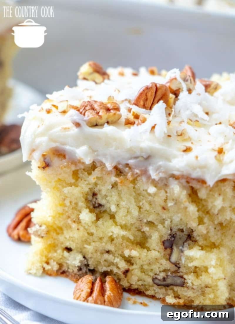 A perfectly baked slice of homemade Italian Buttermilk Cream Cake, adorned with chopped pecans and coconut, resting on a white plate.