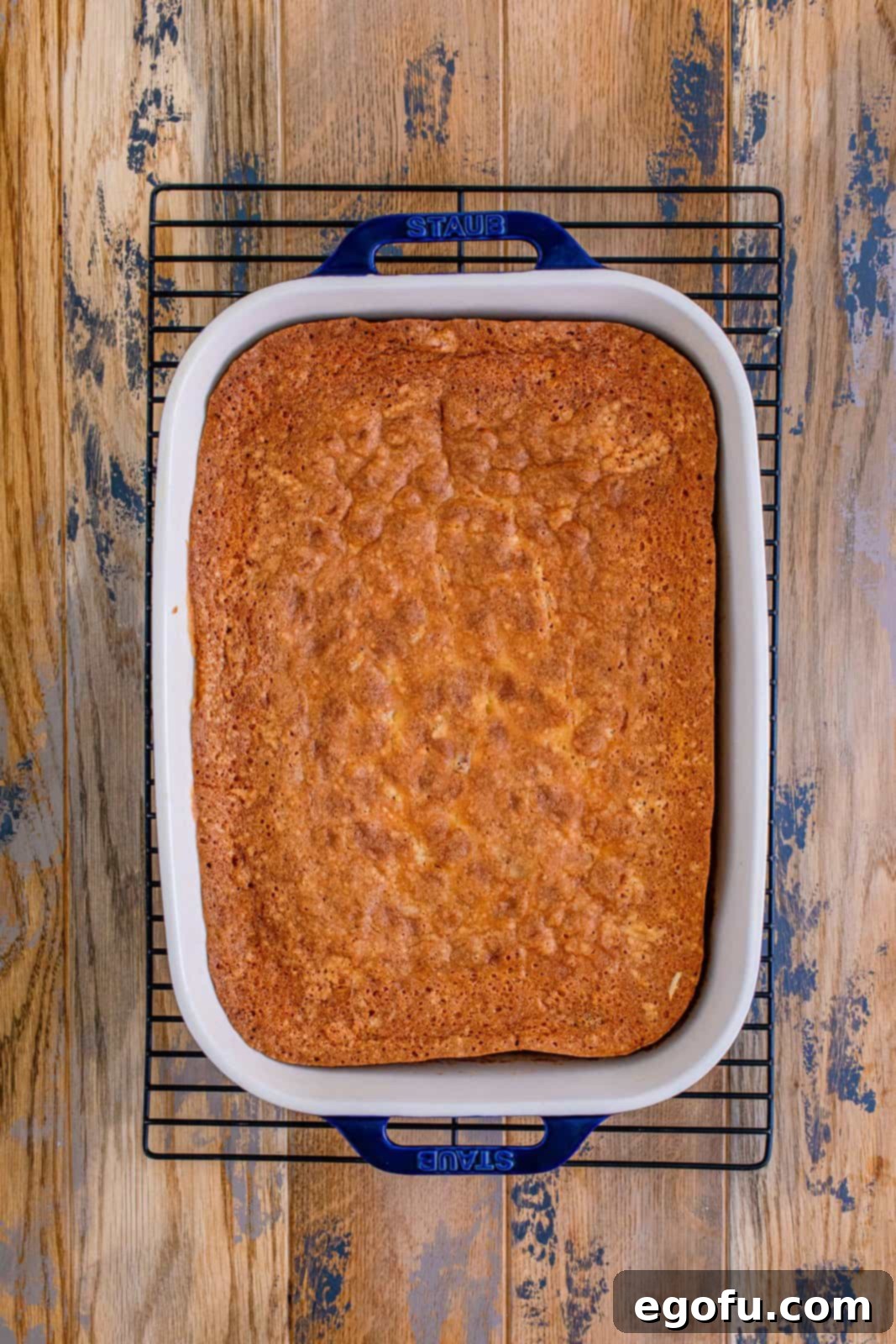 A perfectly baked Italian Cream Cake, golden brown and fluffy, resting in its white baking dish on a cooling rack.